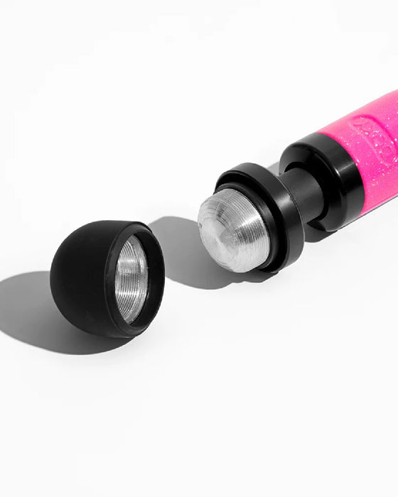 A close-up image of a Doxy Die Cast 3 Compact Wand Vibrator Hot Pink with its black cap removed, revealing the clear lens and led bulb inside, casting a shadow on a white surface.