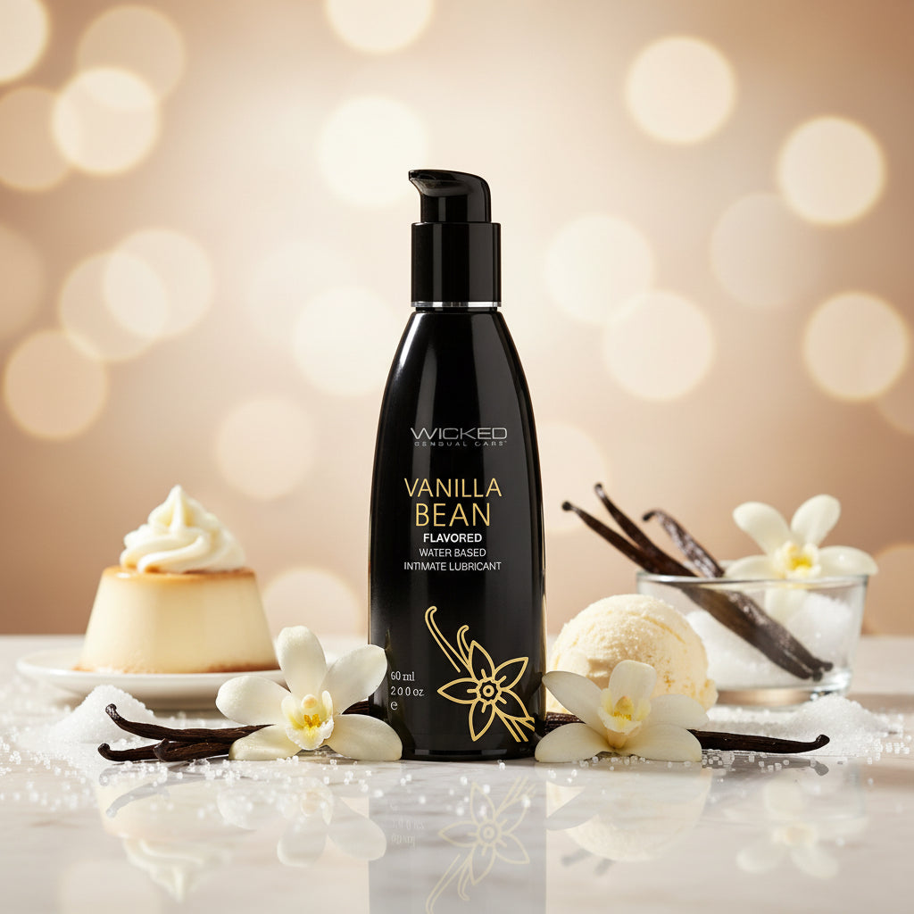 A bottle of Wicked Aqua Vanilla Bean Flavored Water Based Lubricant sits on a gray surface, with blurred glass vases and greenery in the background, bringing a hint of sweetness to your intimate moments.