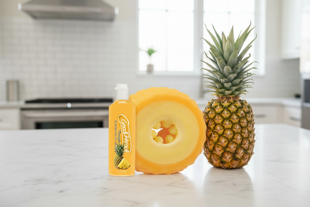 A Goodhead Pineapple Blowjob Set is displayed on a white kitchen counter alongside a round yellow pineapple-shaped soap, a whole pineapple, and an ULTRASKYN stroker, with a blurred modern kitchen in the background.