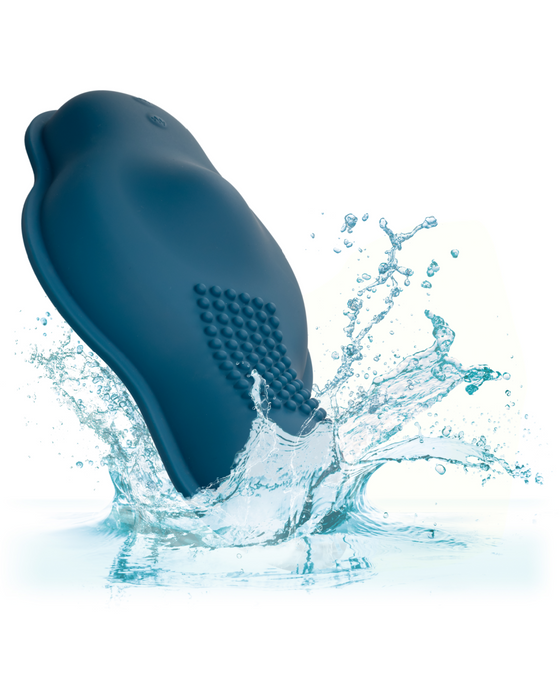 A dark blue, bird-shaped object splashes into clear water, creating droplets and ripples around it. The object, resembling the CalExotics Dual Rider Remote Control Bump & Grind Humping Vibrator with a textured surface, appears to be made of rubber or silicone. The background is white, highlighting the motion and splash effect.
