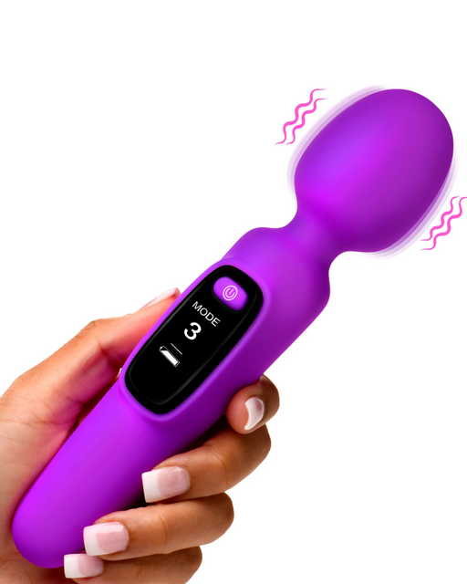 A hand with neatly manicured nails is holding a Bang! First Time Wand Vibrator with Digital Display - Purple by XR Brands, made from body-safe silicone, featuring a small digital screen displaying 'MODE 3.' The massager has a rounded head and wavy lines indicating that it is vibrating.