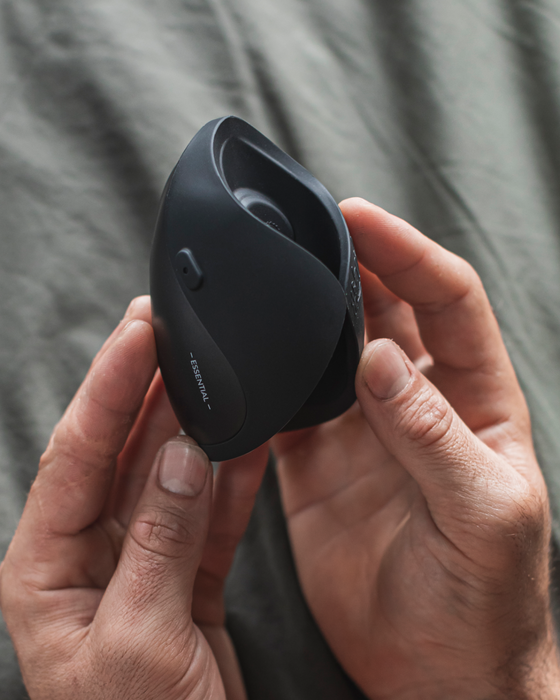 A close-up of hands holding a modern black ergonomic vertical mouse with Hot Octopuss Pulse Solo Essential Oscillating Penis Masturbator Technology over a grey textured background.