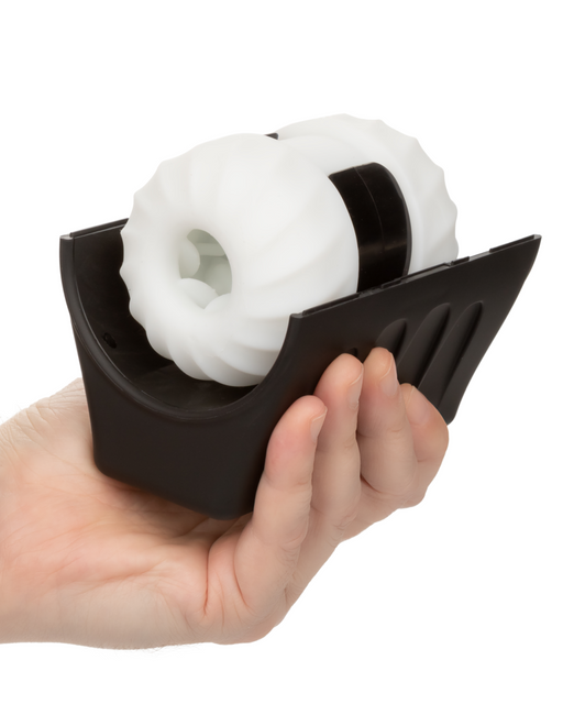 A hand is holding a black plastic holder with two large, white, gear-shaped wheels inside. The holder has ridged sides for easy gripping. The gears are held in place by a black cylindrical axis running through their centers, making it the CalExotics Optimum Power Thruster Stroking Vibrating Penis Masturbator.