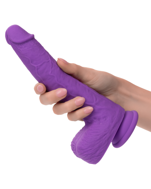 A person holding a CalExotics Silicone Stud Gyrating & Thrusting 9.5 Inch Purple Dildo with a realistic design. The dildo, featuring a textured surface and suction base, also boasts intense action options for added pleasure. With the person's hand gripping it firmly, the plain white background places emphasis on the product.