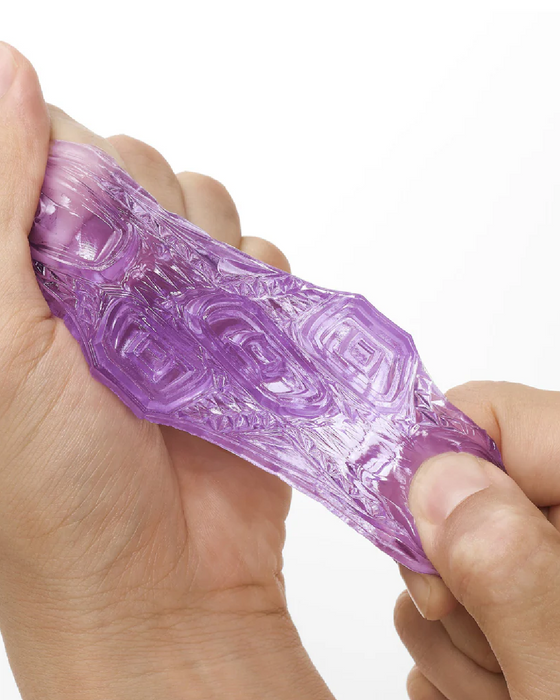 A hand stretching a translucent purple Tenga Uni Topaz Textured Finger Sleeve, showcasing its elasticity and textured surface against a white background.
