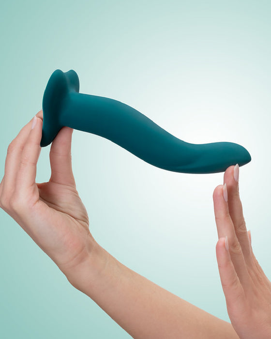 A person holding a Fun Factory Limba Flex Medium Silicone Dildo in Deep Sea Blue against a light blue background. The dildo, designed with a smooth finish and an ergonomic shape, features a suction base.