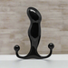 A shiny black, curved object with rounded ends stands upright on a white surface against a light, textured wall—this is the Aneros Progasm Black Ice Hands-Free Prostate Massager (Large), designed for hands-free stimulation.