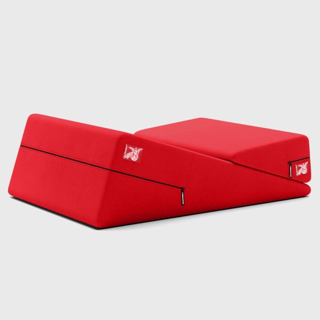 The Liberator Wedge + Ramp Combo – The Iconic Duo for Deeper Pleasure is a red, foldable floor sofa with an angled backrest and seat cushion. It features visible zippers, a small butterfly logo on the front corners, and is set against a light gray background.