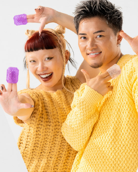 Two cheerful people in yellow sweaters displaying Tenga Uni Variety Pack Textured Finger Sleeves for Stroking and Clit Massage, making playful poses against a white background.