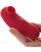 A hand holding a red silicone REMI 15-Function Rechargeable Remote Control Suction Panty Vibe with a hollow opening at one end by Maia Toys.