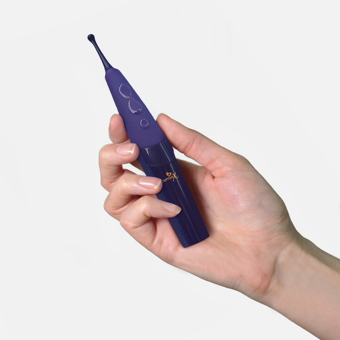 A hand holds a Zumio X2 Rotating Clitoral Stimulator with a dark purple curved SpiroTip, shown against a plain white background.