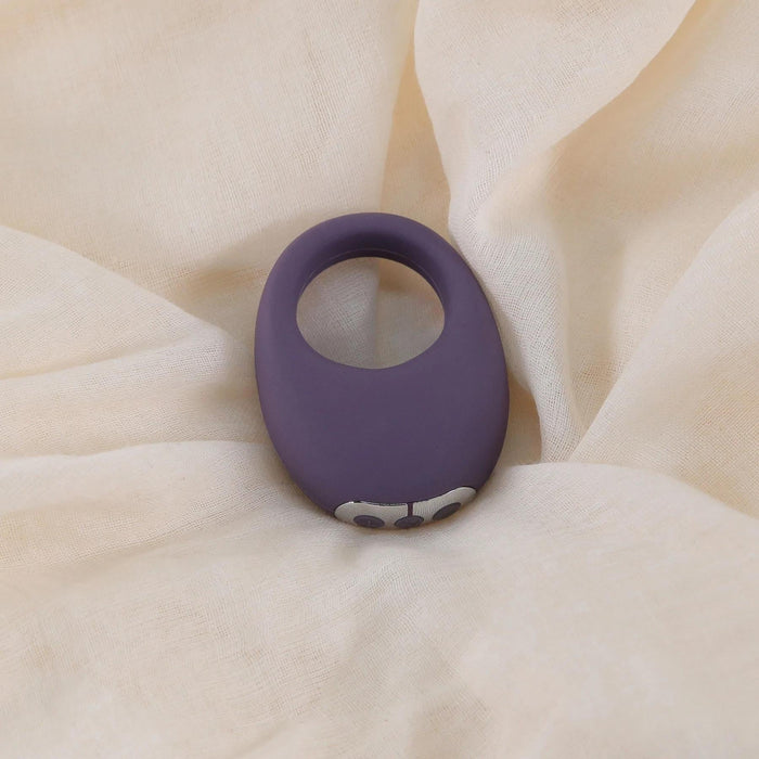 Purple silicone Mio vibrating cock ring with silver buttons, on a cream fabric background.