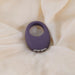 Purple silicone Mio vibrating cock ring with silver buttons, on a cream fabric background.