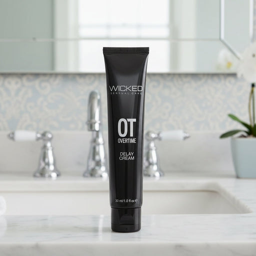 A black tube labeled "Wicked Overtime Ejaculation Delay Gel for the Penis" stands upright on a white bathroom countertop, with a sink, faucets, and mirror in the background.