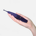 A hand holds the Zumio X2 Rotating Clitoral Stimulator, a dark purple device with a slim design and SpiroTip, set against a plain light background.
