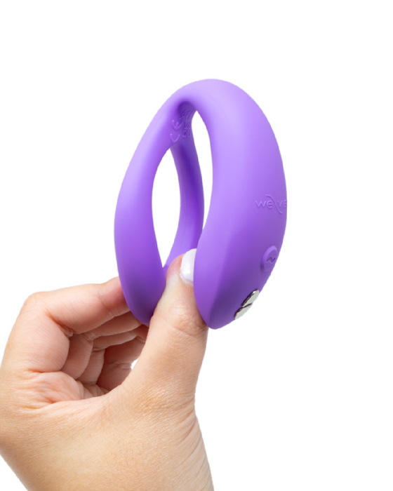 A hand holding a We-Vibe Sync O Hands-Free Wearable Couples Vibrator - Purple against a white background.
