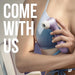 A person in a blue sports bra holds the Satisfyer Pro 2 Waterproof Pressure Wave Clitoral Stimulator - Lilac near their chest. Bold white text on the left reads "COME WITH US." The scene is softly lit with a minimal, modern background.