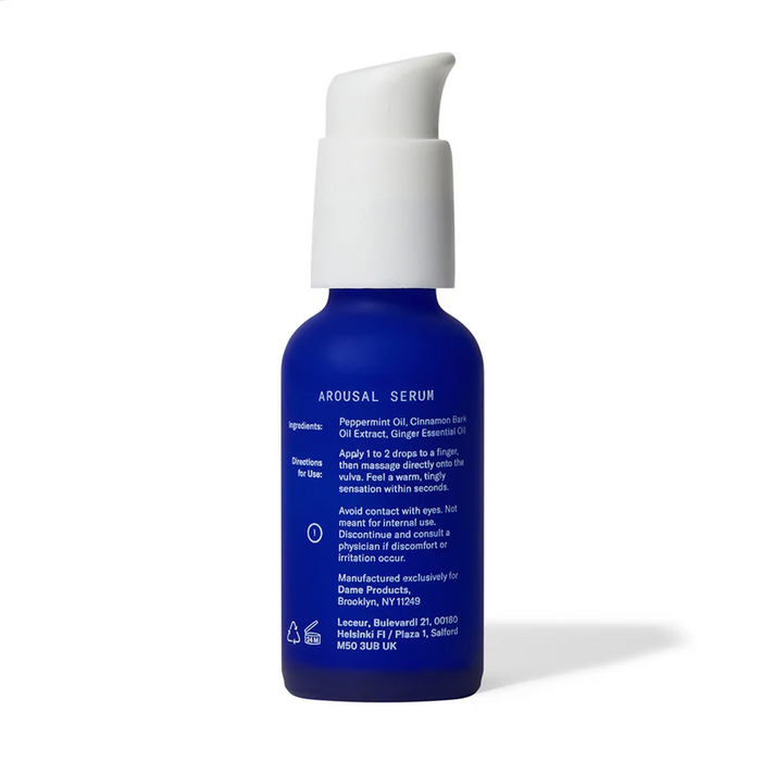 A blue bottle of Dame Lickable Clitoral Arousal Serum 1 oz with a white pump stands upright. The label features ingredients, directions, and caution info. Formulated for clitoral stimulation with a natural formula, it's set against a plain background.