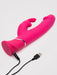 The Happy Rabbit Dual Density Rechargeable Silicone Rabbit Vibrator, featuring dual stimulation arms in pink, rests on a white surface with its USB charging cable attached.