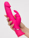A hand holds the Happy Rabbit Dual Density Rechargeable Silicone Rabbit Vibrator, a bright pink lifelike silicone toy with a curved design and smaller external stimulator, against a plain light background.