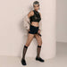 A person with short, two-toned hair confidently poses against a light wall, wearing the Strap On Me Allure Boxer Style Harness with a sheer black crop top, high-waisted black shorts, an open beige jacket, knee-high sheer socks, and black loafers.
