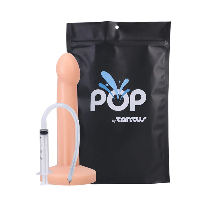 The Pop 7 Inch Silicone Squirting Dildo - Vanilla, a realistic flesh-toned toy with syringe and tube for squirting action, is shown before black packaging labeled “POP by Tantus.” This harness-compatible dildo offers versatile play options.