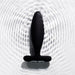 The Je Joue Vesta Petite Powerful Remote Control Vibrating Butt Plug—a black, body-safe silicone, T-shaped toy—stands upright on a textured white surface, creating ripples that suggest its waterproof design.