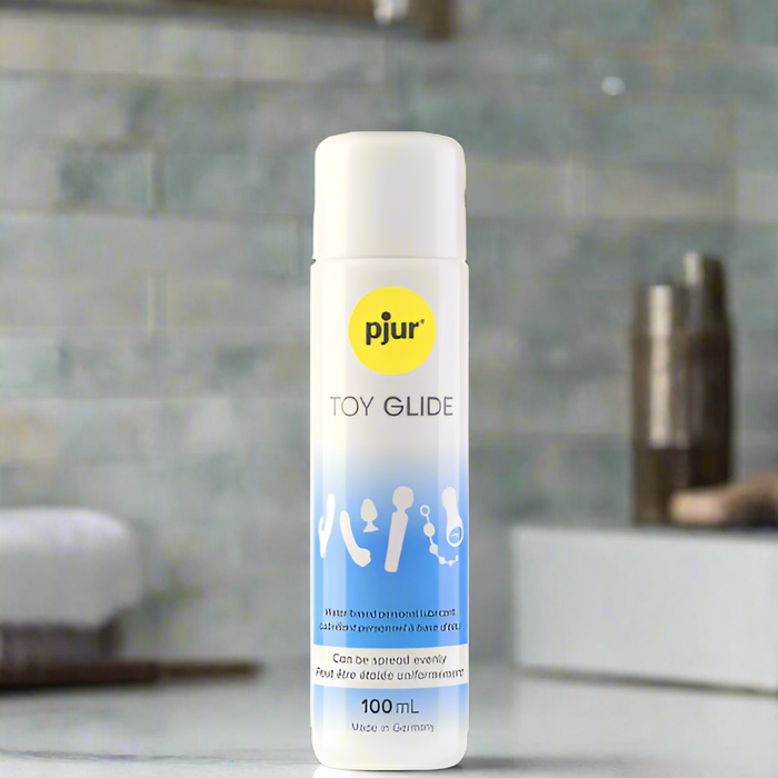A 100 mL Pjur Toy Glide Water Based Lubricant for Sex Toys stands upright on a bathroom counter with a blurred background—ideal for smooth, long-lasting lubrication with your favorite toys.