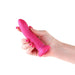 A hand with pink-painted nails holds the Charlie 5 inch Small Silicone Dildo in Metallic Pink, featuring a strong suction cup base, against a white background.