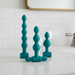 The Bumpy 3-Piece Beaded Anal Plug Set with Vibrating Bullet includes three teal beaded plugs of various sizes and shapes, each displayed upright, with one plug featuring a removable vibrating bullet for customizable pleasure.