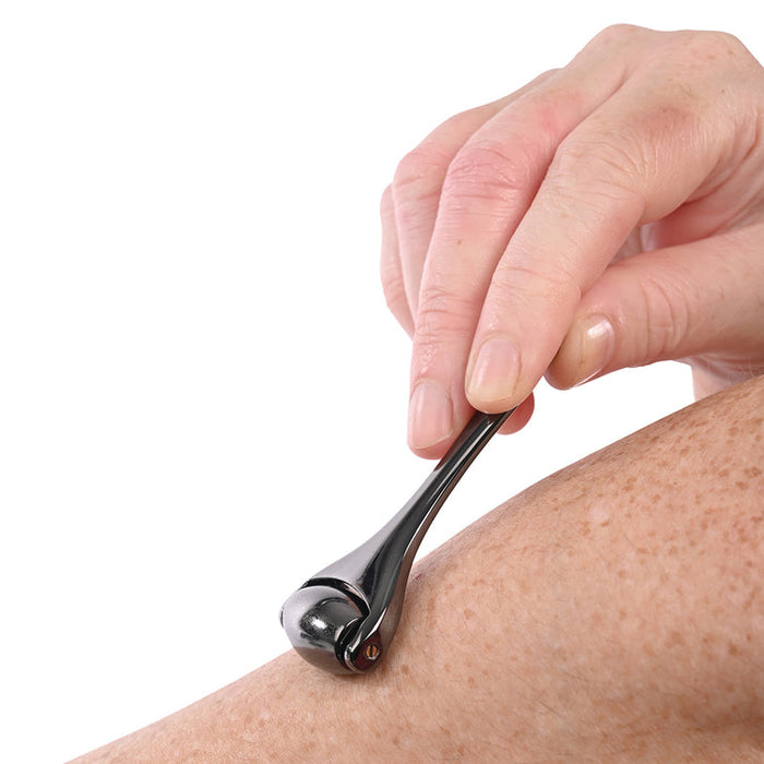 A hand uses the Ex's & Oh's Temperature Play Sensory Roller on a freckled forearm, inviting an intimate exploration of erotic sensation against a plain white background.