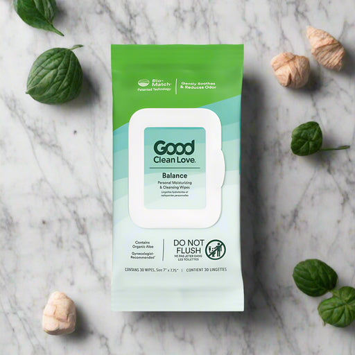 A 30-count pack of Good Clean Love Balance Personal Moisturizing & Cleansing Wipes is shown on marble with green leaves and dried beige flowers. The pH balanced packaging features aloe, freshness, and a "Do Not Flush" label.
