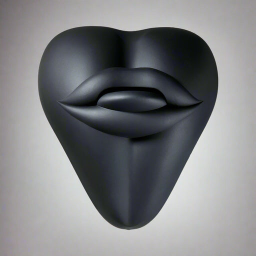 The Bananapants Kissi Dildo Base features a black, sculptural heart shape with abstract lips and tongue on its surface. Crafted from body-safe silicone, it's shown against a white background.