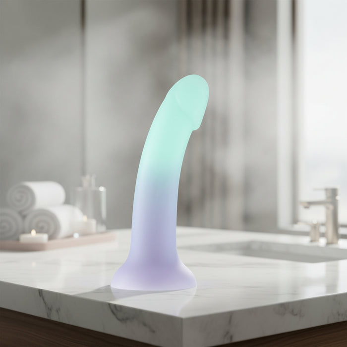 The Ombre Curve Liquid Silicone 6 Inch Slim Dildo, featuring an ombré pastel design, realistic shape, flared suction cup base, and G-Spot stimulation, is displayed on a white background.