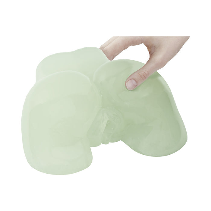 A hand stretches and squeezes the Glow-in-the-Dark Peek-A-Booty Masturbator, a soft, translucent, pale green model shaped like buttocks, showing off its flexibility and realistic texture.