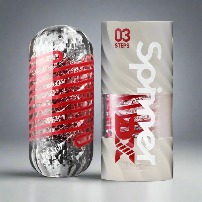 The Tenga Spinner DX Steps Textured Masturbator, a transparent cylindrical toy with red spirals, is shown beside its white packaging labeled "03 Steps" and "Spinner," emphasizing its spiral motion design for men.