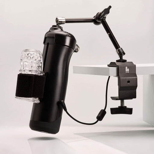 The Handy Handsfree Desk Mount features a black cylindrical device with a clear textured sleeve, secured by a strap and mounted to a white table with an articulating arm for adjustable positioning.