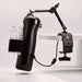 The Handy Handsfree Desk Mount features a black cylindrical device with a clear textured sleeve, secured by a strap and mounted to a white table with an articulating arm for adjustable positioning.