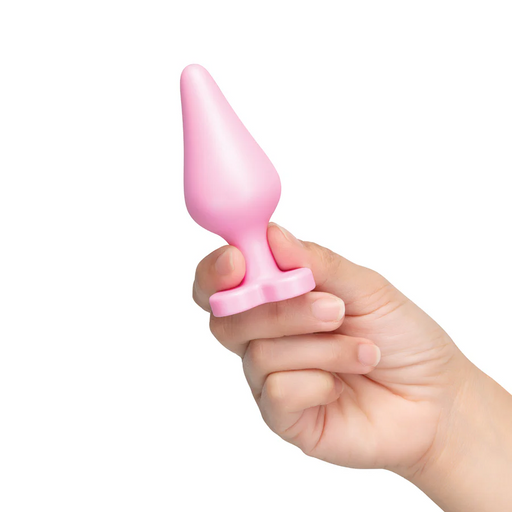 Hand holding a small, pink silicone butt plug with a tapered bulb and a heart-shaped flared base.