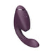 The Womanizer Next Duo Pleasure Air + Vibration Blended Orgasm Stimulator, a dark purple, curved vibrator with side control buttons, is shown on a white background and features 3D Pleasure Air technology for blended orgasms.