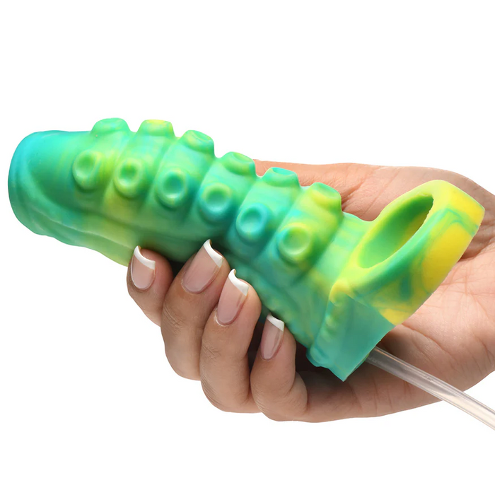 A hand holds the Siphon Green Tentacle Squirting Penis Enhancer, a silicone sleeve in green and yellow with raised bumps and a circular opening.