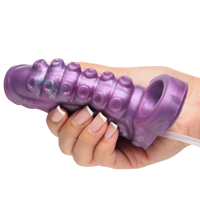 A hand holds the Siphon Tentacle Squirting Purple Penis Enhancer, a textured silicone sleeve with circular bumps and a hollow opening at one end.