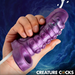 A hand holds the Siphon Tentacle Squirting Purple Penis Enhancer with a shiny, textured surface as white fluid squirts from its tip. A swirling blue background and bold "CREATURE COCKS" text amplify its fantasy-themed allure.