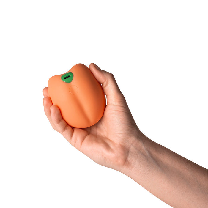 A hand holds the Emojibator Peach Vibrating Penis Stroker—a peach-shaped, waterproof sex toy—against a white background.