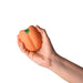 A hand holds the Emojibator Peach Vibrating Penis Stroker—a peach-shaped, waterproof sex toy—against a white background.