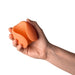 A hand holds the Emojibator Peach Vibrating Penis Stroker—an orange, flexible, silicone stroker with a ribbed interior—against a white background.