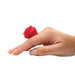 A hand with manicured nails wears the Bloomgasm Rose Ring Finger Vibrator, made from body-safe silicone, on the middle finger against a white background.