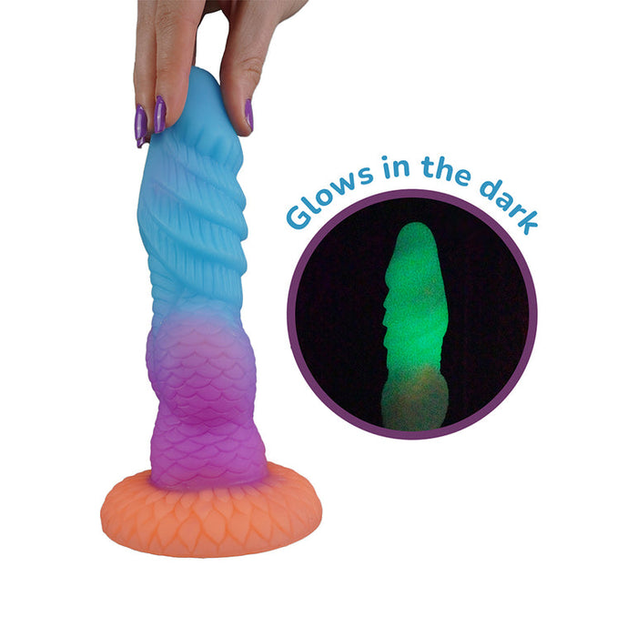 A hand holds the Splash Nova Squirting 10 Inch Glow in the Dark Creature Dildo, featuring a mermaid-inspired design and suction base. An inset reveals it glowing green in the dark. Text reads "Glows in the dark.