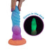 A hand holds the Splash Nova Squirting 10 Inch Glow in the Dark Creature Dildo, featuring a mermaid-inspired design and suction base. An inset reveals it glowing green in the dark. Text reads "Glows in the dark.