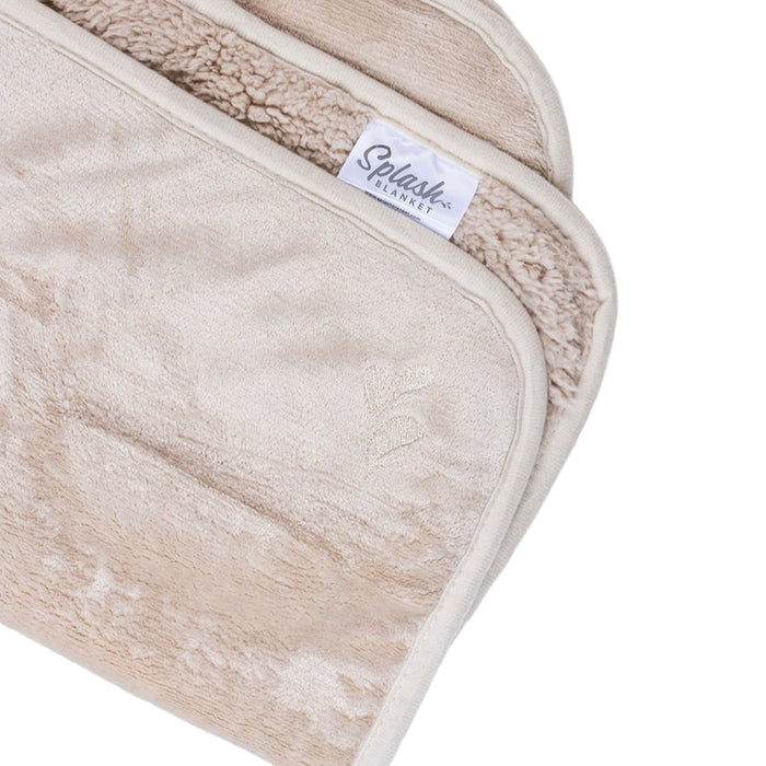 A close-up of the Splash Blanket The OG Waterproof Blanket - Medium, featuring a soft beige plush texture, absorbent material, subtle embroidered heart detail, and a sewn-in label.
